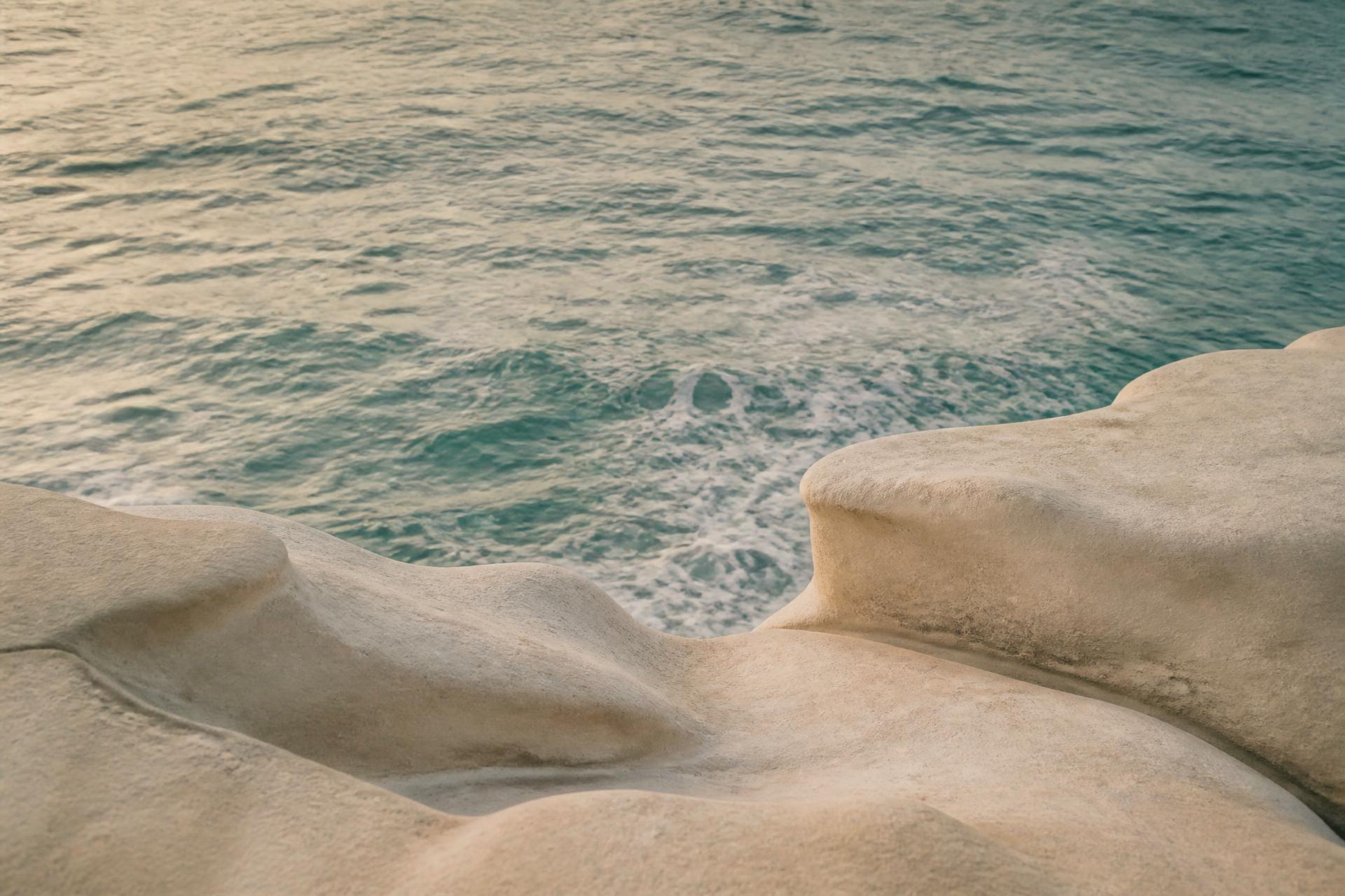 Calm Mediterranean sea meeting pale sculpted stone at dawn
